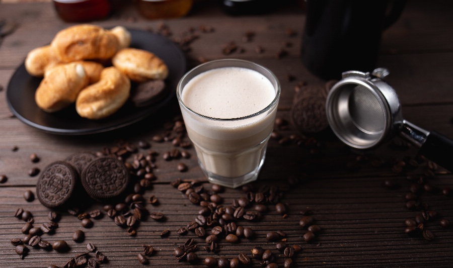 Apsveikuma e-kartiņa Piena glāze uz galda blakus būlciņām un kafijas graudiem