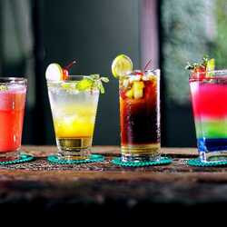Apsveikuma e-kartiņa: Četras krāsainas alkohola glāzes uz galda