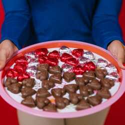 Apsveikuma e-kartiņa: Persona tur paplāti ar sirdsveida šokolādes konfektēm