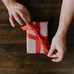 Apsveikuma e-kartiņa: Vīrietis gatavo dāvanu ar sarkanu lentīti
