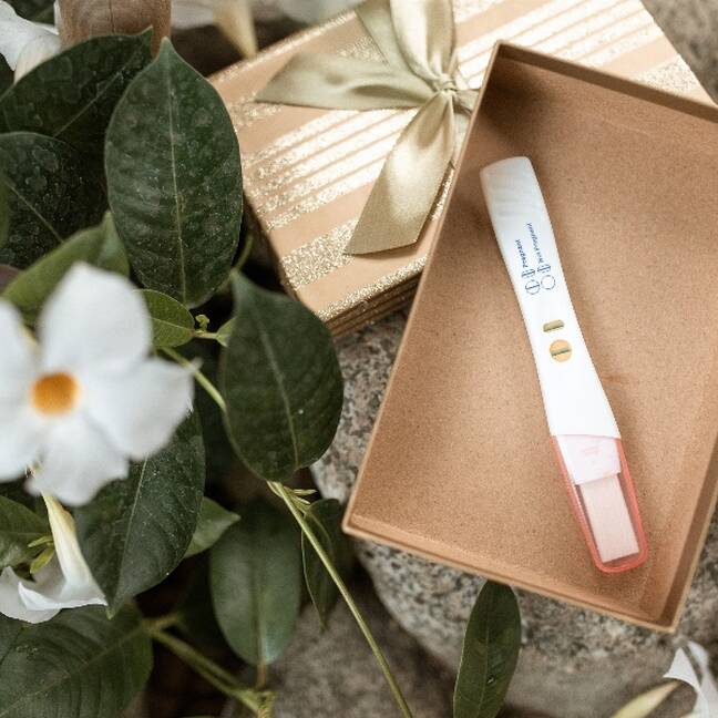 Baltas puķes blakus kastītei ar pozitīvu grūtniecības testu Bērniņa piedzimšana e-kartiņa