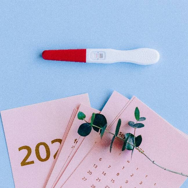 Pozitīvs grūtniecības tests un kalendārs uz zila fona e-kartiņa